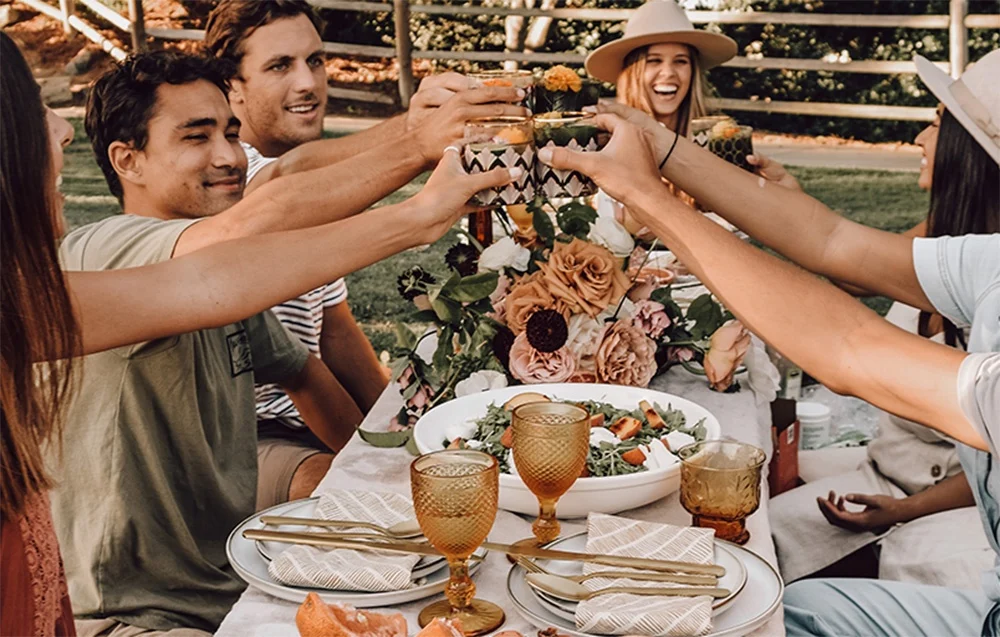 Παρέα φίλων απολαμβάνει picnic σε εξωτερικό χώρο με ποτά και σαλάτα στο τραπέζι